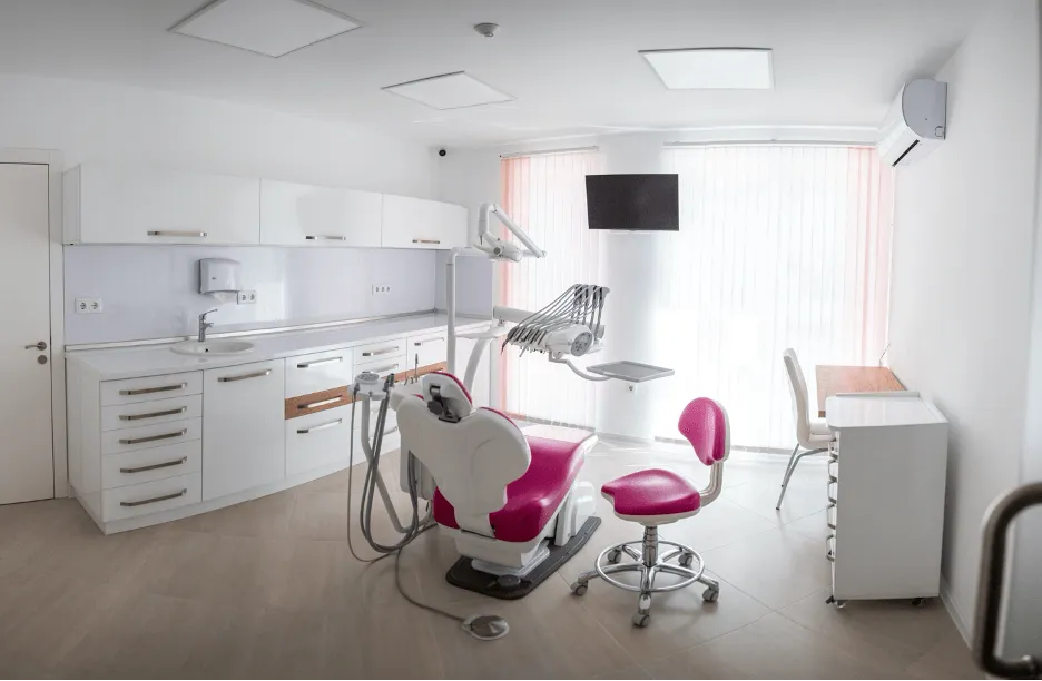 Стоматологичен кабинет с розово кресло и мивка, готов за лечение на пациенти.